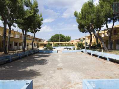 Una piccola salita ci immette ora in un ampio largo rettangolare di un azzurro sbiadito, circondato da basse palazzine palazzine giallo-ocra tutte uguali, collegate in alto da un unico grande ballatoio e rette da un porticato che corre per i lati pi� lunghi. Siamo davanti al primo nucleo di abitazioni nato a Enziteto